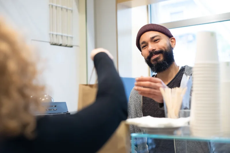A small business owner handing a purchase across the counter to a customer