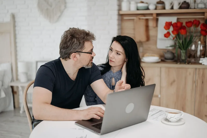 A couple reviewing a plan together on a laptop at their kitchen table