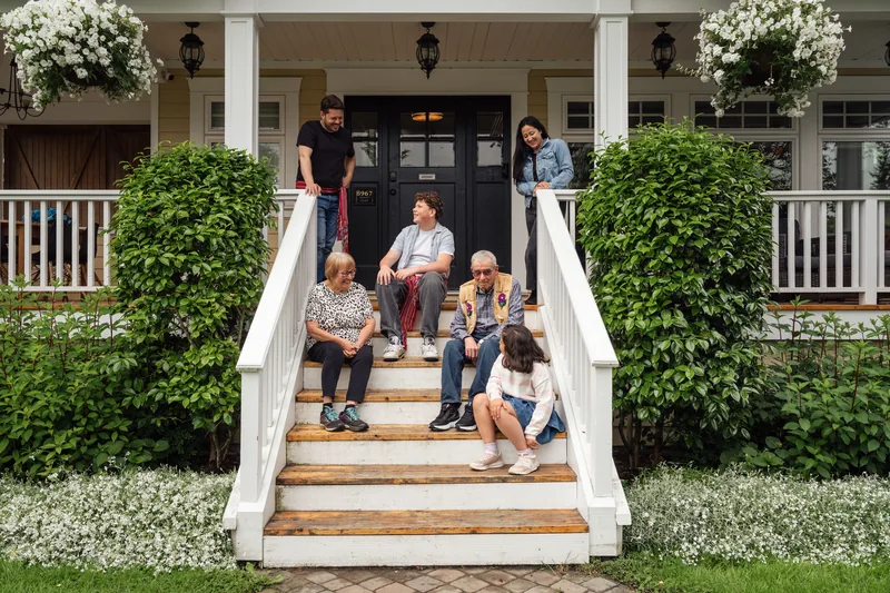 A multigenerational family gathered on the front steps of a white porch