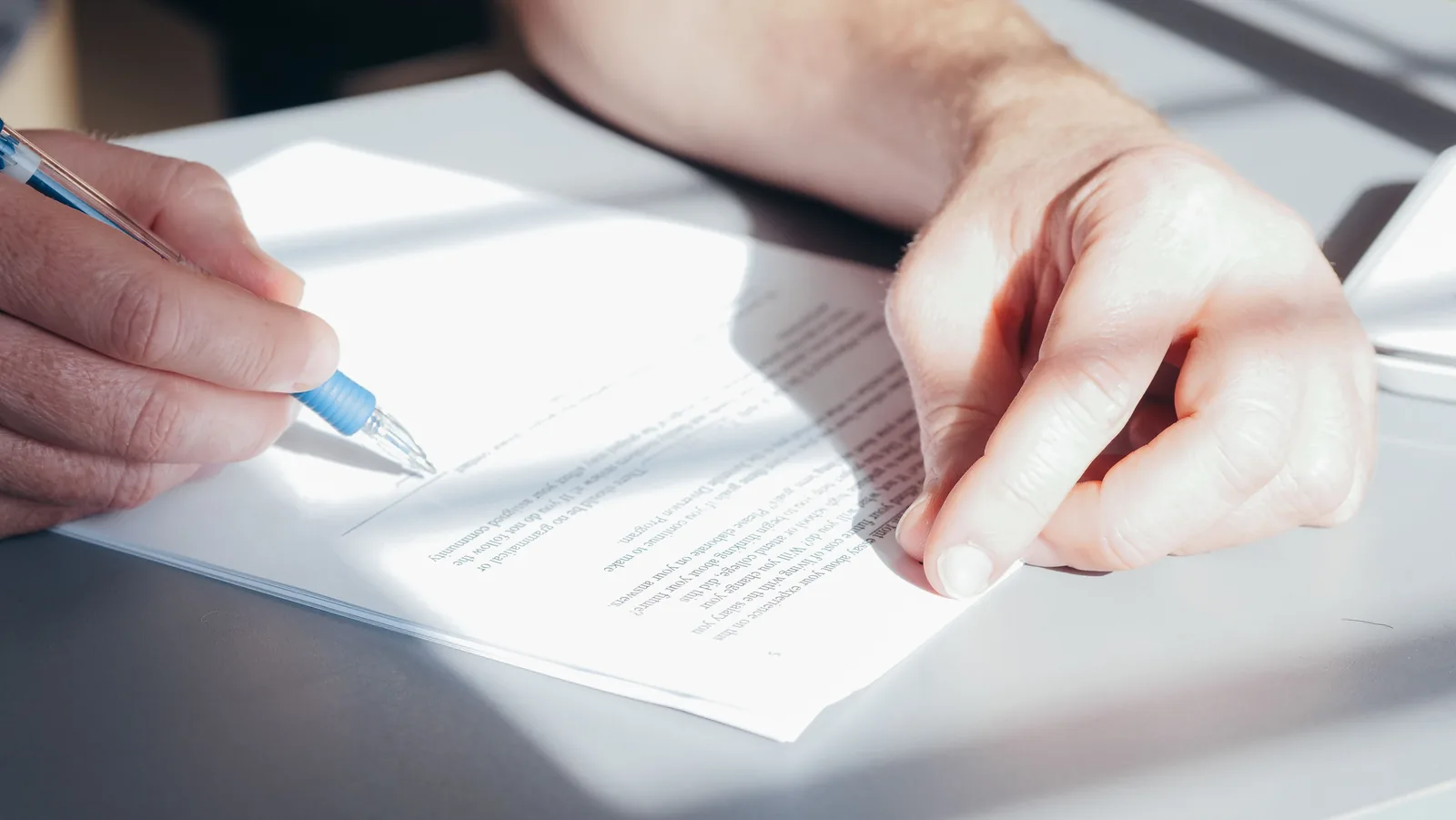 Hands signing a legal document with a pen at a bright desk