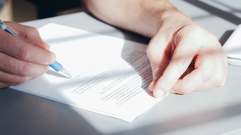 Hands signing a document with a pen on a bright desk